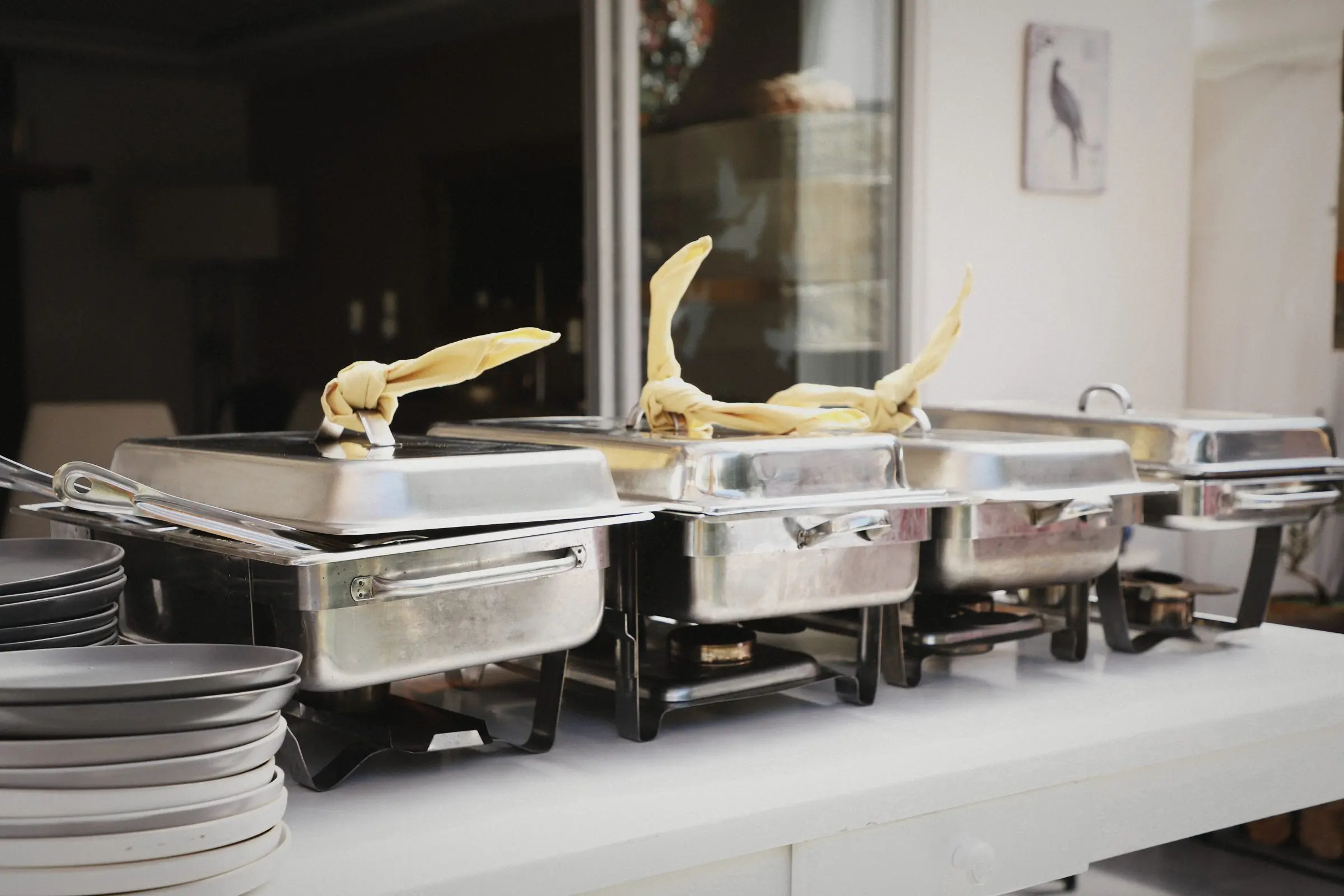 A row of steel chafing dishes and stacked plates ready for service.